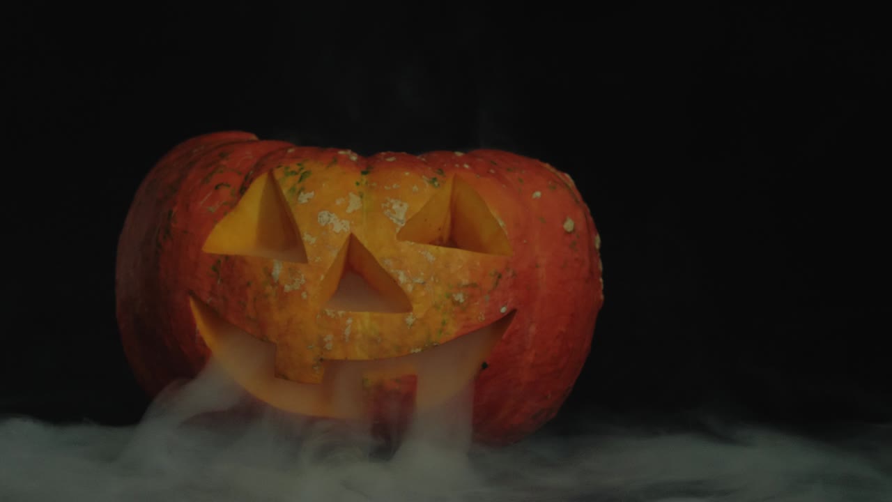 cargada halloween calabaza jack-o-lanterna con velas en ella en la mesa oscura con humo blanco. la luz está parpadeando lentamente. cámara lenta. disparo de primer plano. 4k