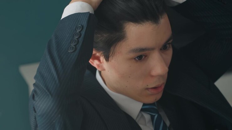 Giovane uomo d'affari che si sistema i capelli, scrivania d'ufficio tranquilla con pianta e laptop, cura attenta e compostezza nervosa mentre si prepara per un colloquio, illuminazione sottile evidenzia la trama dell'abito.