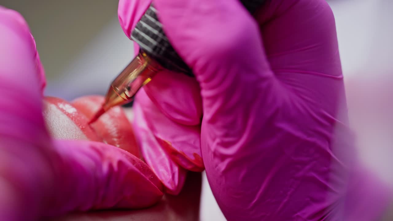 Permanent make-up on lips. Cosmetology procedure. Hands in pink gloves applying red permanent tattoo on girl's lips. Close-up.