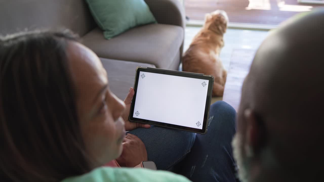 Couple holding tablet on couch, leaning in and inspecting blank screen corner marks for setup