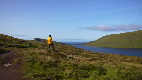 hombre con impermeable amarillo admirando el paisaje verde y volcánico de las islas feroe en leitisvatn