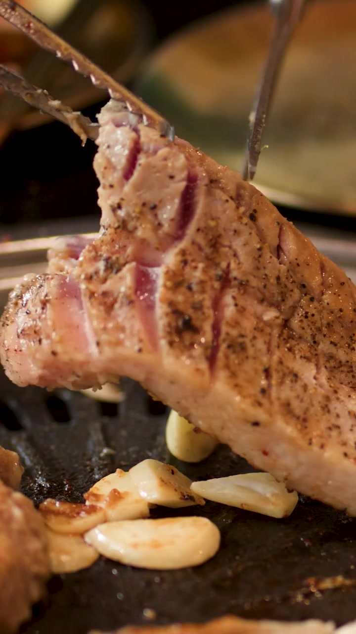 Primo piano verticale di mani che usano forbici e pinze per tagliare carne di maiale su una griglia