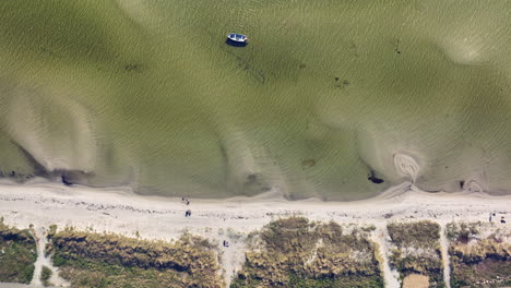 Eine-Luftaufnahme-Eines-Einsamen-Bootes,-Das-In-Der-Nähe-Eines-Sandstrandes-Vor-Anker-Liegt.-Das-Klare,-Seichte-Wasser-Lässt-Die-Muster-Des-Meeresbodens-Und-Die-Spärliche-Unterwasservegetation-Erkennen