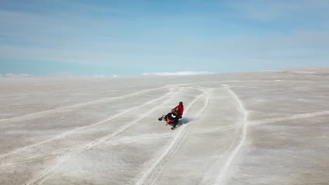 Aerial-view-of-a-person-doing-stunts-on-a-snowmobile,-on-the-surface-of-a-glacier-in-Iceland,-on-a-bright-sunny-day
