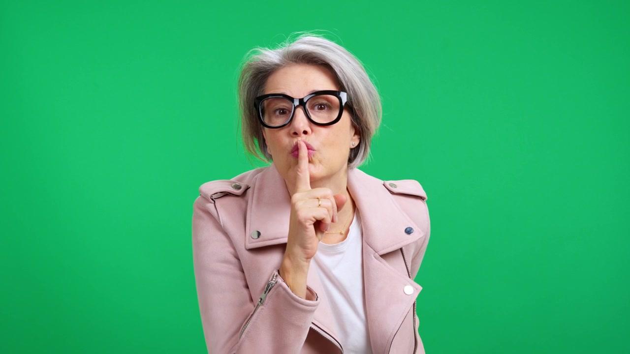 Mujer mayor elegante haciendo el gesto de silencio en pantalla verde