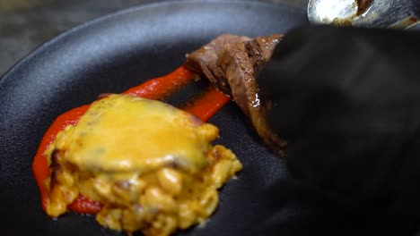 poniendo una rebanada de carne en un plato negro con macarrones y queso