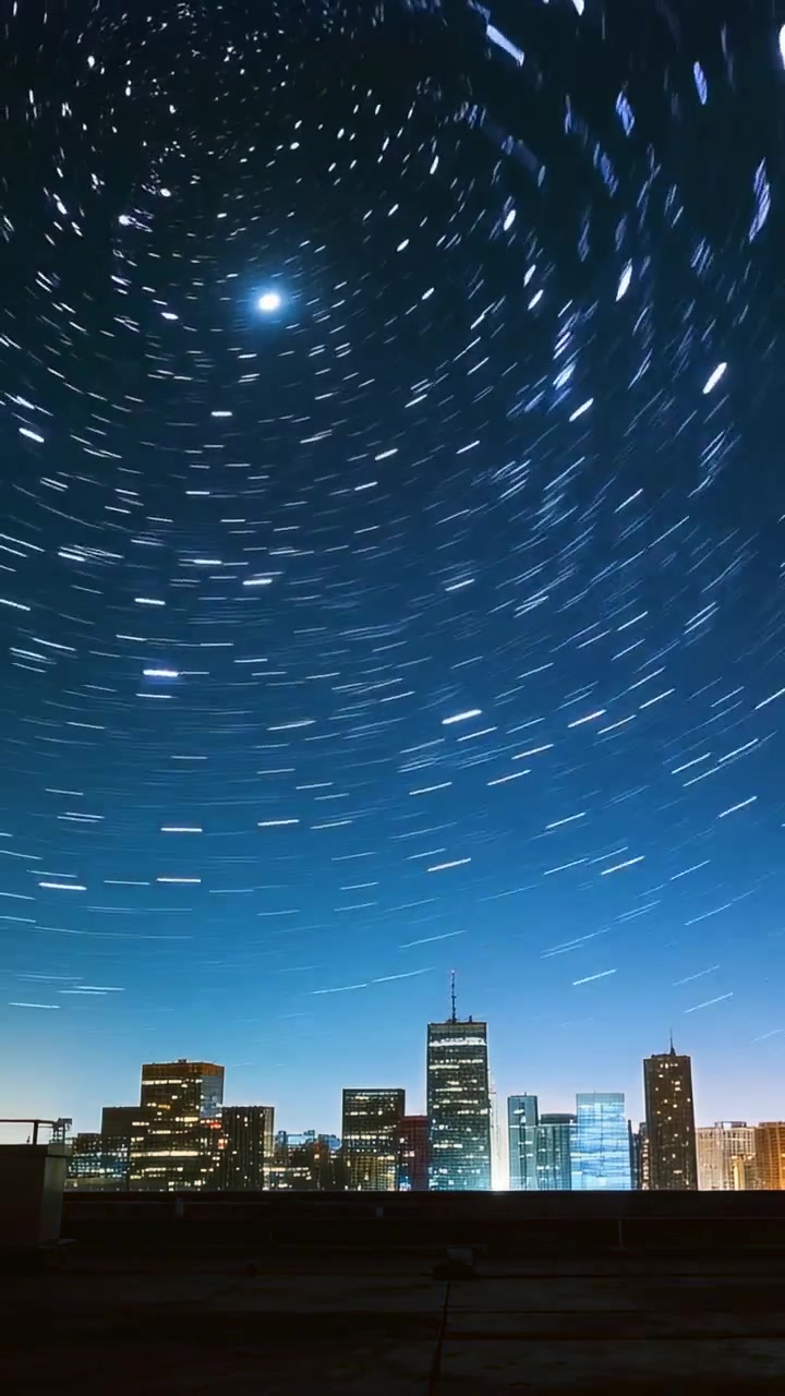 Video verticale: Telecamera che riprende un timelapse di scie stellari rotanti sopra lo skyline da un tetto con una stella luminosa.
