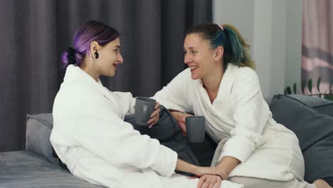 happy pregnant woman and her girlfriend spending time together at home in bathrobe