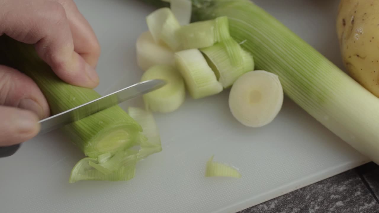 Hand slicing leek vegetable with knife close up overhead shot