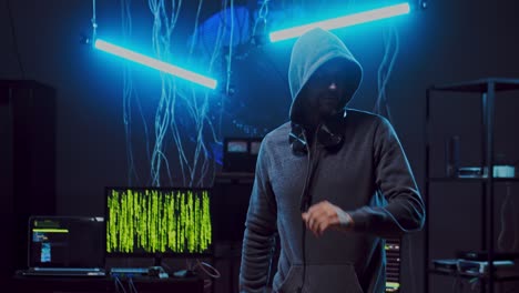 joven hacker en un capó escuchando música y bailando en la oscura sala de neón con cables