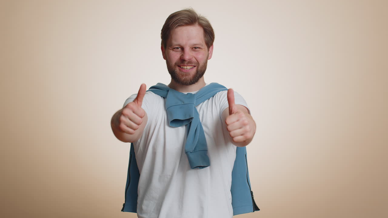 Happy young man raises thumbs up agrees or gives positive reply recommends advertisement likes good