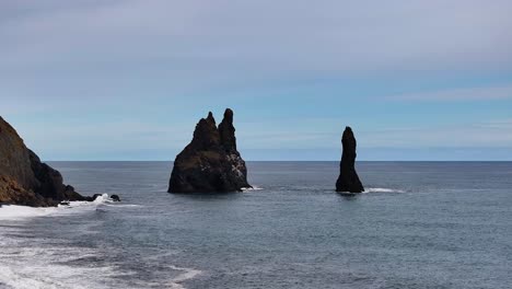 two majestic mountains rise from the sea, their presence mirrored in the gentle waves that softly caress the black sand beach, creating a serene sense of stillness