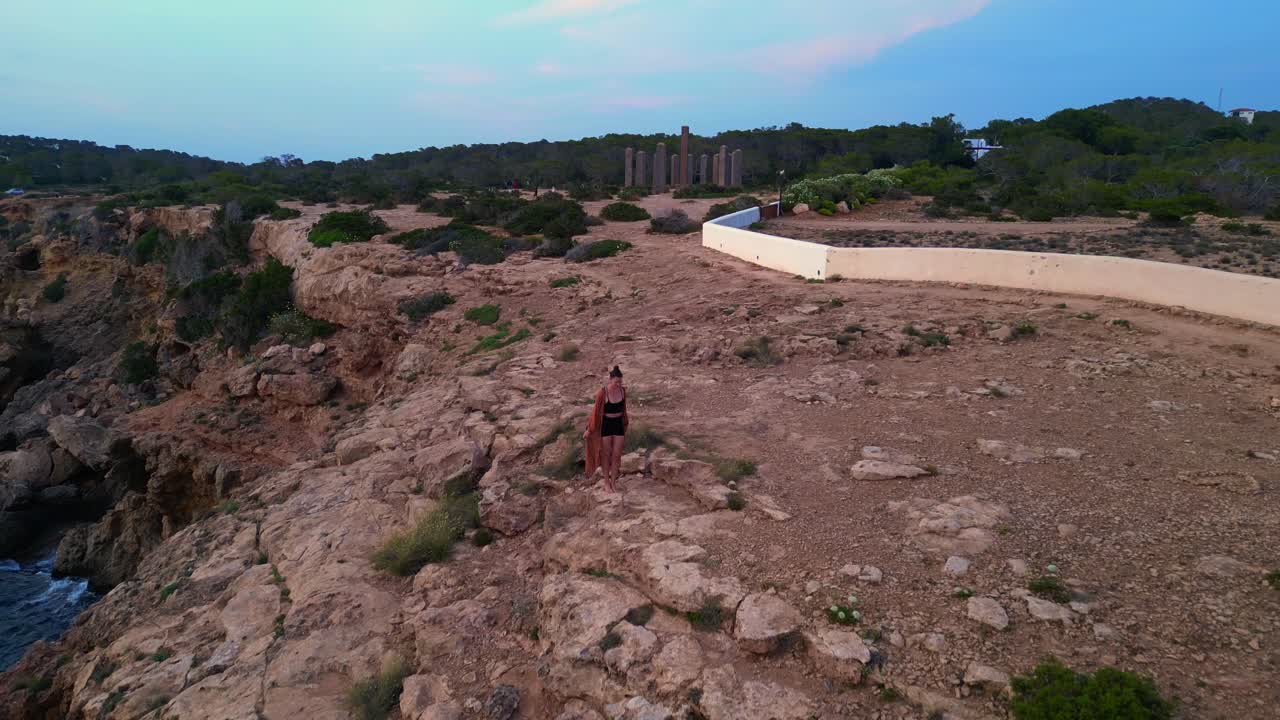 dancing Woman expressing freedom and movement by the sea at a beautiful travel destination Cala Llentia Ibiza. Gorgeous aerial view flight fly reverse drone