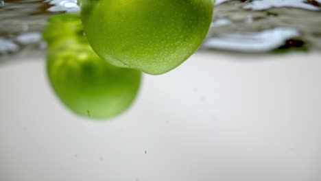 Two-fresh-green-apples-floating-with-bubbles-towards-water-surface