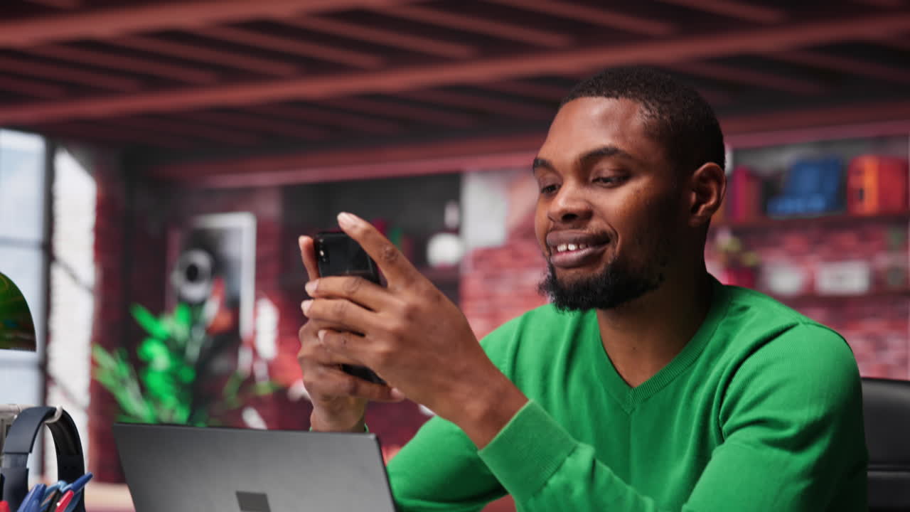 Young adult reading messages on mobile phone in his loft apartment