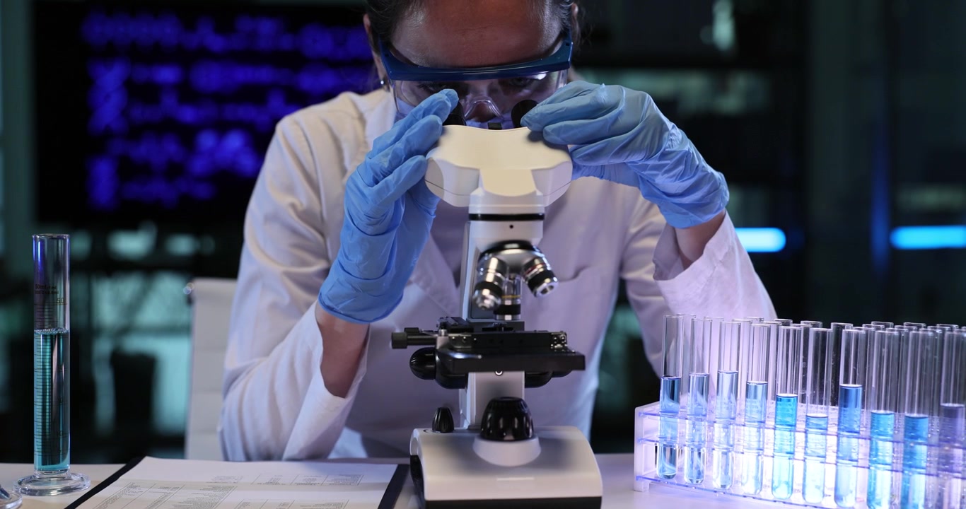 Woman scientist adjusts microscope for work during lab test