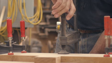 a carpenter tightens a vice holding boards of wood together in slow motion