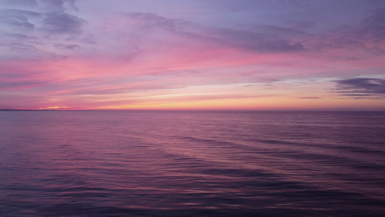 Ascesa di un drone su un mare calmo su cui il sole tramonta in un tramonto magico dai colori pastello intensi.