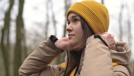 a young girl puts on her yellow woolen hat in the forest