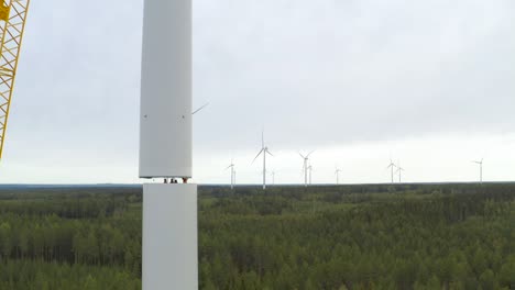 group of workers assembling the parts of a wind turbine mast during construction with a crane, drone shot