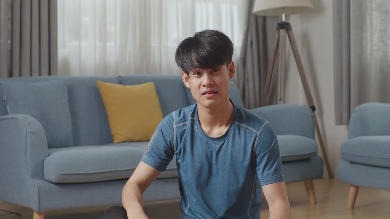 운동복을 입은 운동체조의 아시아인 남자가 집에서 운동을 마친 후 미니멀한 인테리어를 가진 넓고 은 거실에서 포즈를 취하고 있습니다.