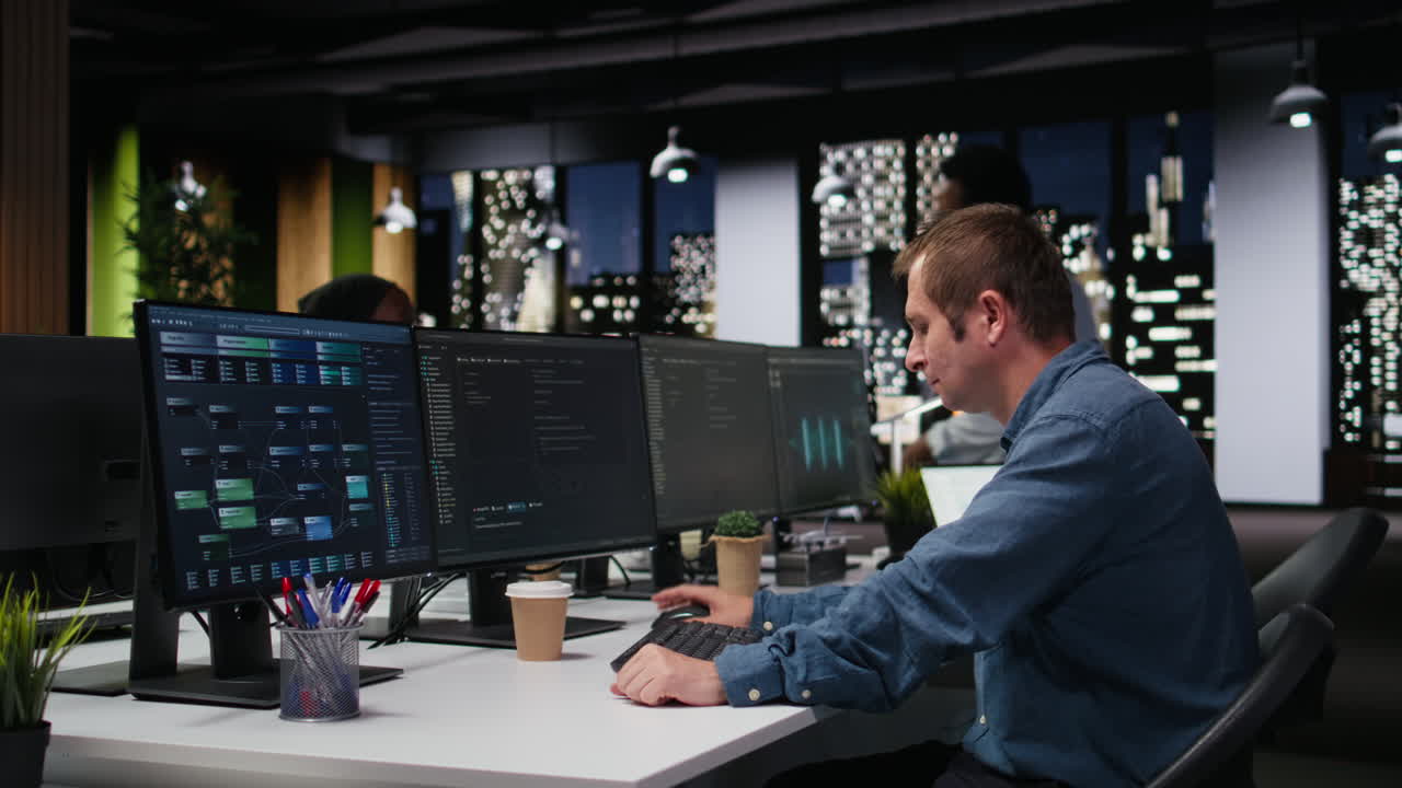 Mannlig programmerer jobber med flere dataskjermer på et moderne kontor om natten