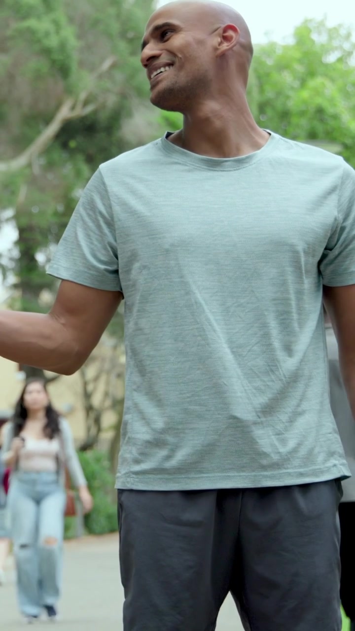 Video vertical: Hombre en forma jadeando, revisando su reloj inteligente después de terminar de correr por un sendero del parque, vistiendo una camiseta