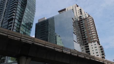 a building on sukhumvit street with the bts elevated railway, blue sky and clouds, bangkok, thailand