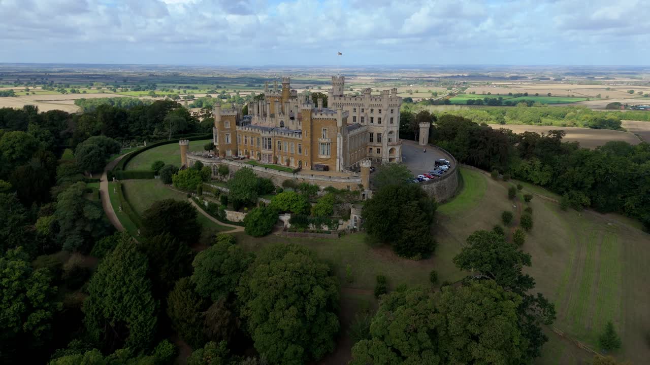 Scenic aerial drone view of stone castle surrounded by green terrain and rural farmland in East Midlands, England