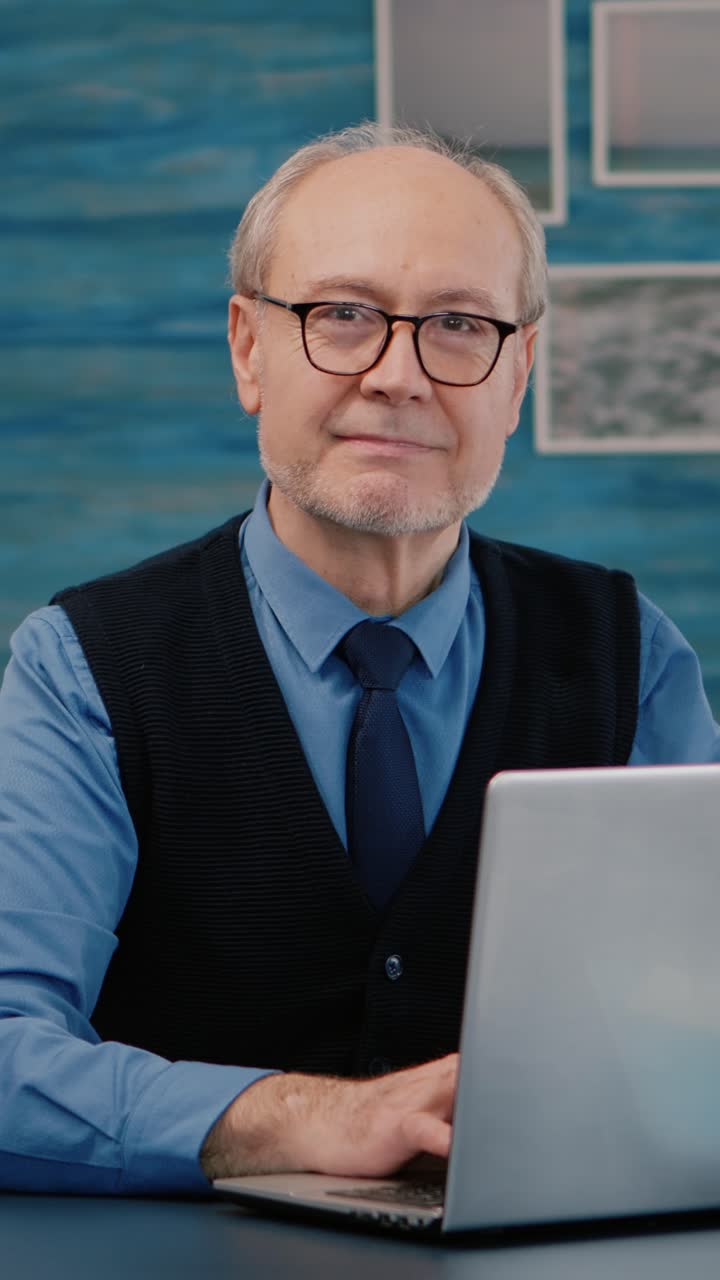 Vertical video: Retired manager sitting at desk in front of camera smiling