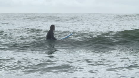 sportive man in wetsuit with artificial leg lying on surfboard and swimming in the ocean