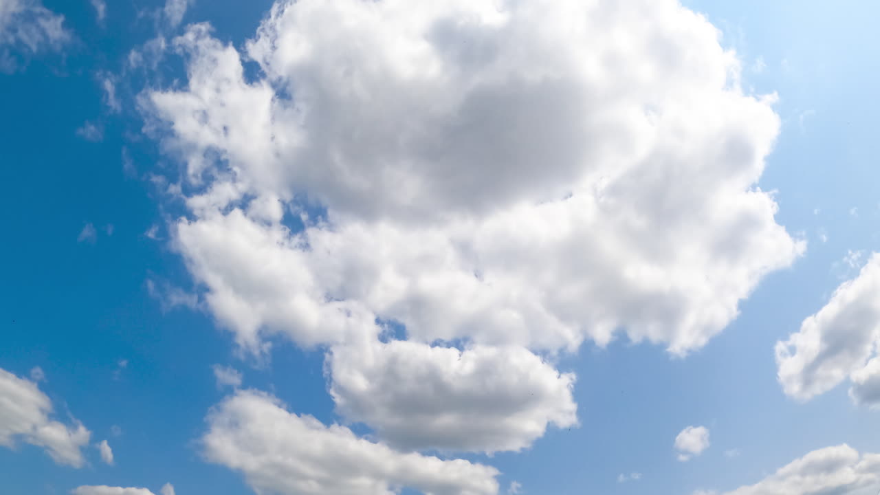 Light blue summer sky with occasional white clouds appearing and transforming. Bright sun shining on the cloudscape. Low angle view timelapse.