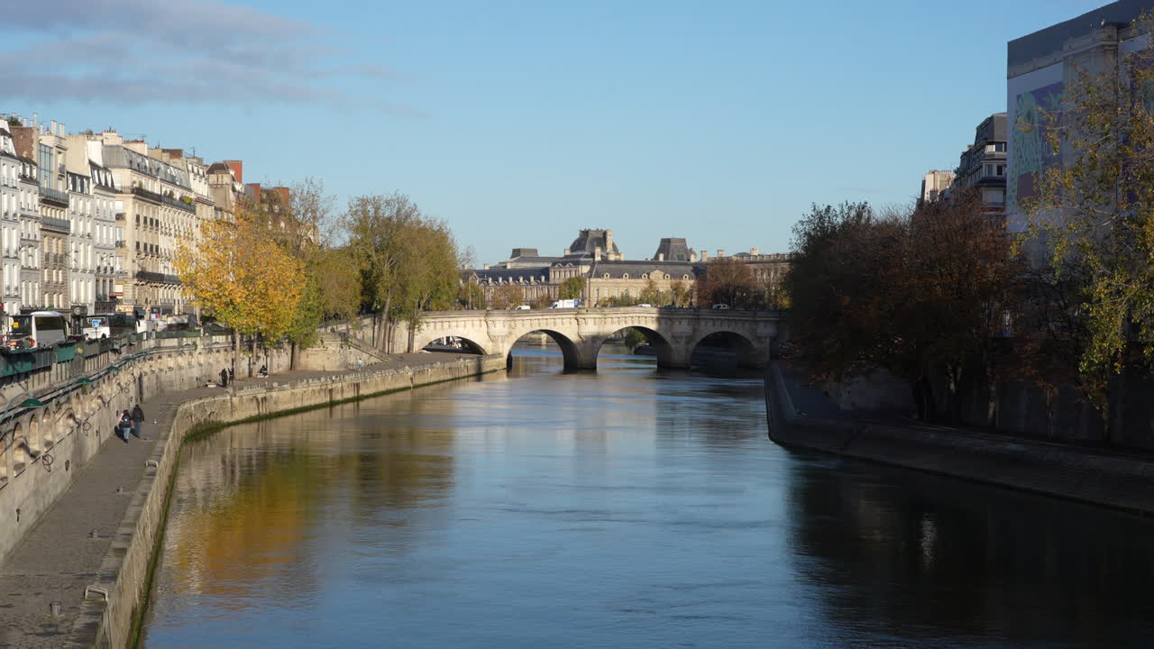 View of Pont Saint-Michel bridge over the Seine River in Paris on a sunny autumn day. Warm light on the calm water as trees and classic Parisian buildings line the riverbanks, peaceful cityscape