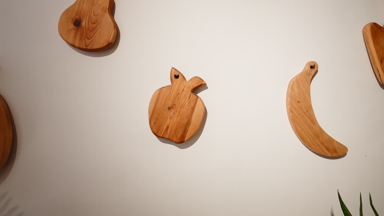 Taglieri in legno a forma di frutta appesi a una parete bianca