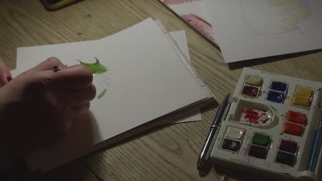 Female-hands-paint-green-holly-leaves-on-a-handmade-Christmas-card-in-Close-up