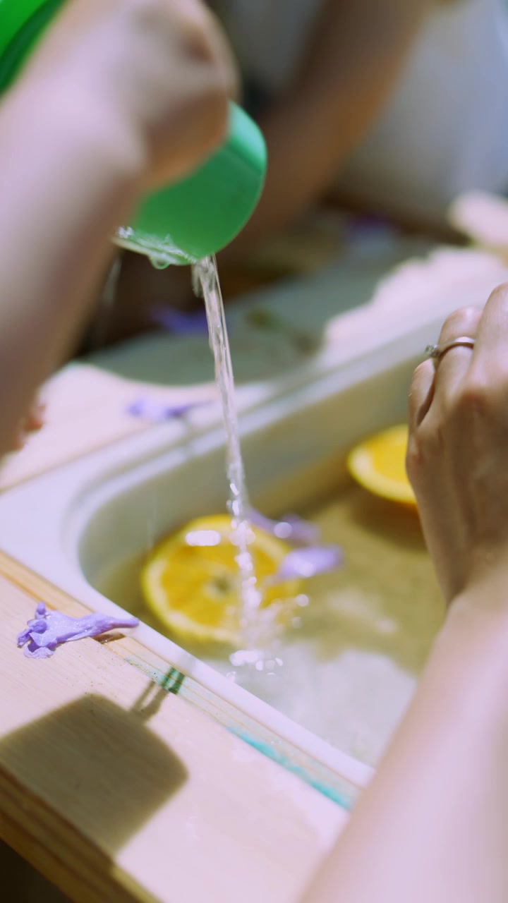 Manos de niño vertiendo agua con rodajas de naranja en juego sensorial