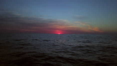 Deep-dark-blue-panoramic-ocean-view-from-a-drone-with-a-vivid-red-shining-sun