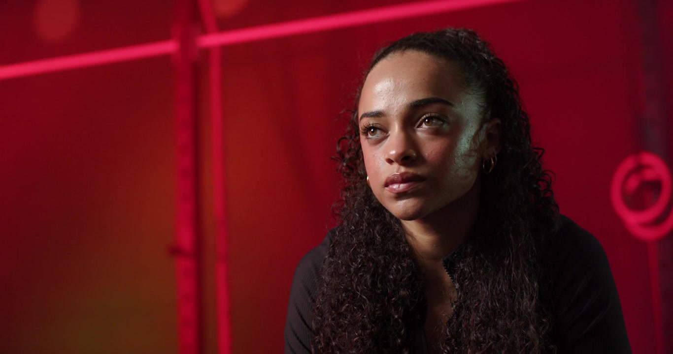 Mujer afroamericana reaccionando a una señal fuera de cámara, desviando la mirada a la derecha, estructura de escenario roja, espacio para texto.