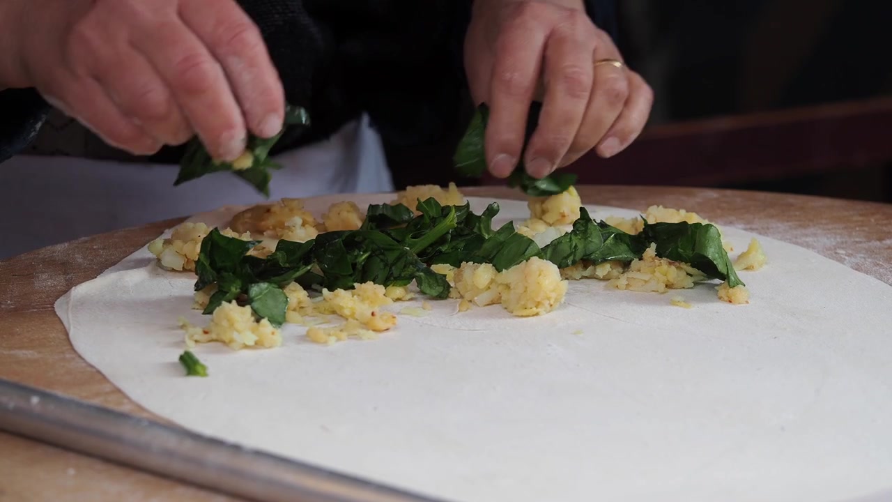 Chef che prepara una focaccia tradizionale con ripieno di spinaci e patate.