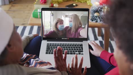 african american mother and daughter using laptop for christmas video call with family on screen