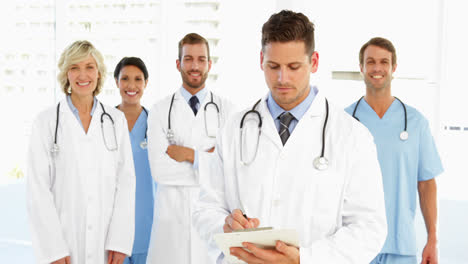 el médico escribe en el clipboard mientras el personal está de pie detrás de él