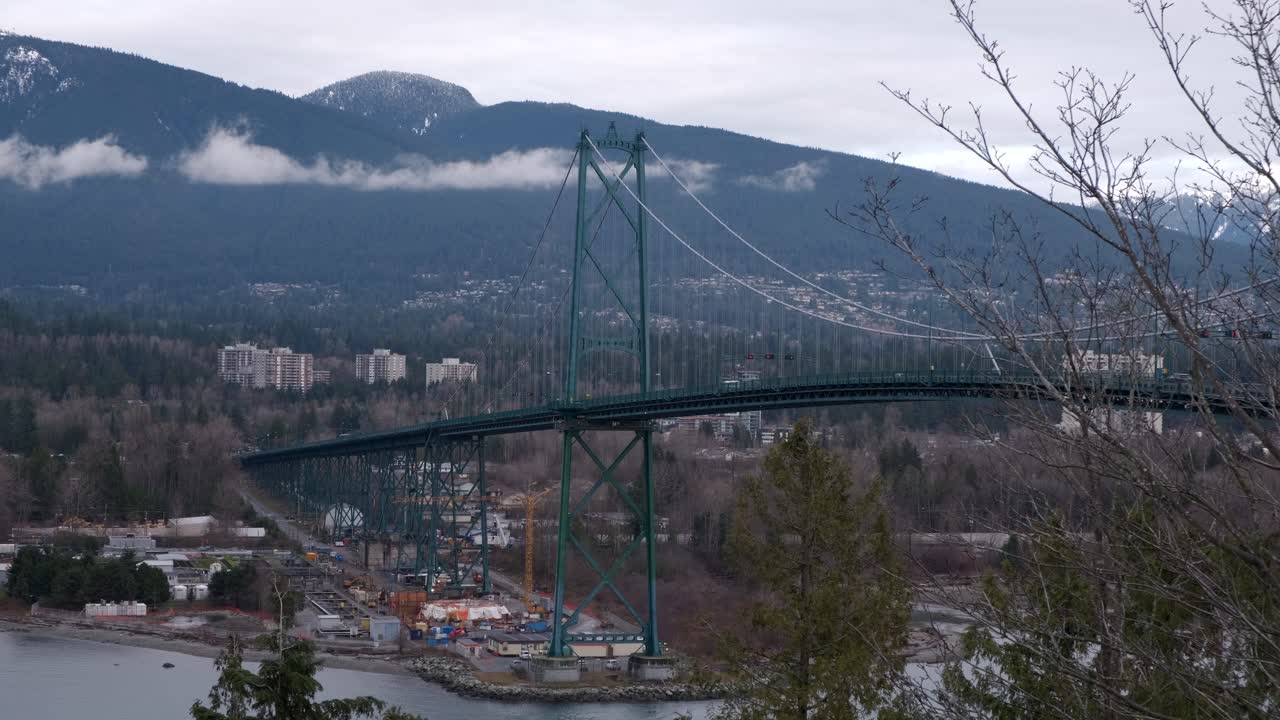 Cars driving on the Lions Gate bridge in Vancouver, BC with mountains in the background on a cloudy winter day (4K)