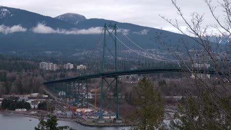cars driving on the lions gate bridge in vancouver, bc with mountains in the background on a cloudy winter day (4k)