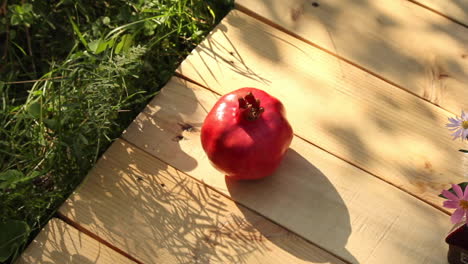 single ripe red pomegranate on wood decking next to grass in sunny garden