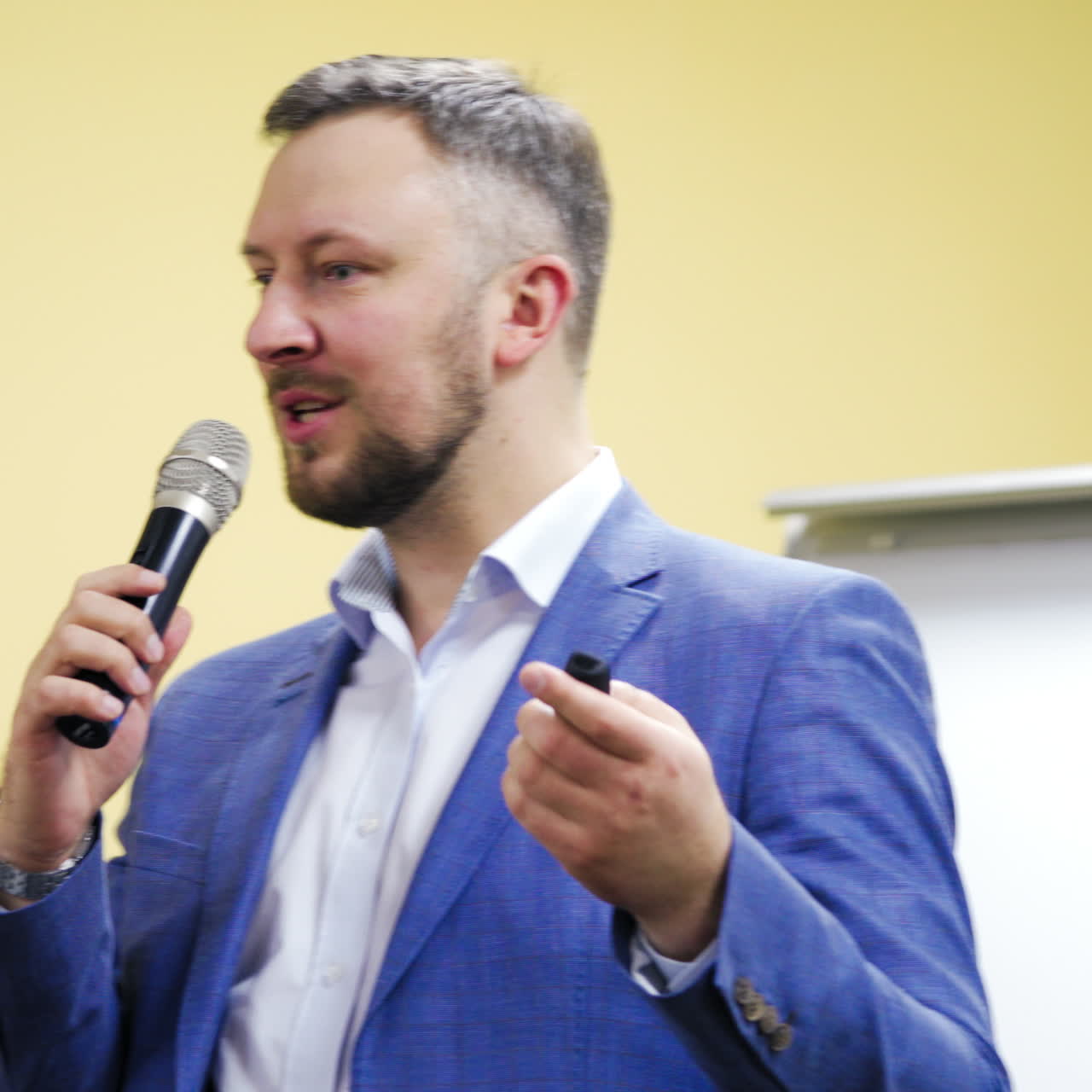 Bearded businessman is speaking to the mic on the light hall background. Handsome entepreneur leading the meeting during important symposium indoors.