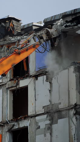 Tall building destroyed by an earthquake. Demolition machine tearing down roof of a wrecked building. Long machine claw pulling down the debris. Vertical video