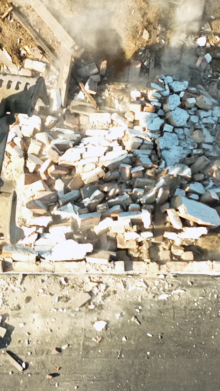 A highangle aerial shot shows a hydraulic excavator claw breaking down a brick wall at a construction site. Useful for urban development and industrial demolition projects