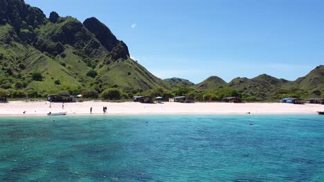 tourist walking on popular pink beach with sandy coastline and crystal clear turquoise ocean water within komodo national park, indonesia