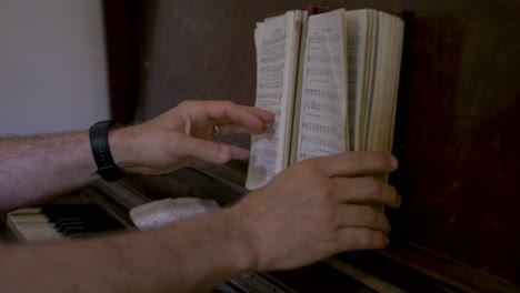 un pianista hojeando las páginas de un libro de himnos en un viejo piano de madera antiguo