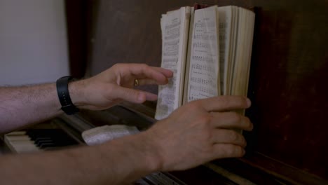 a pianist flipping through pages of a hymnal book on an old antique wooden piano